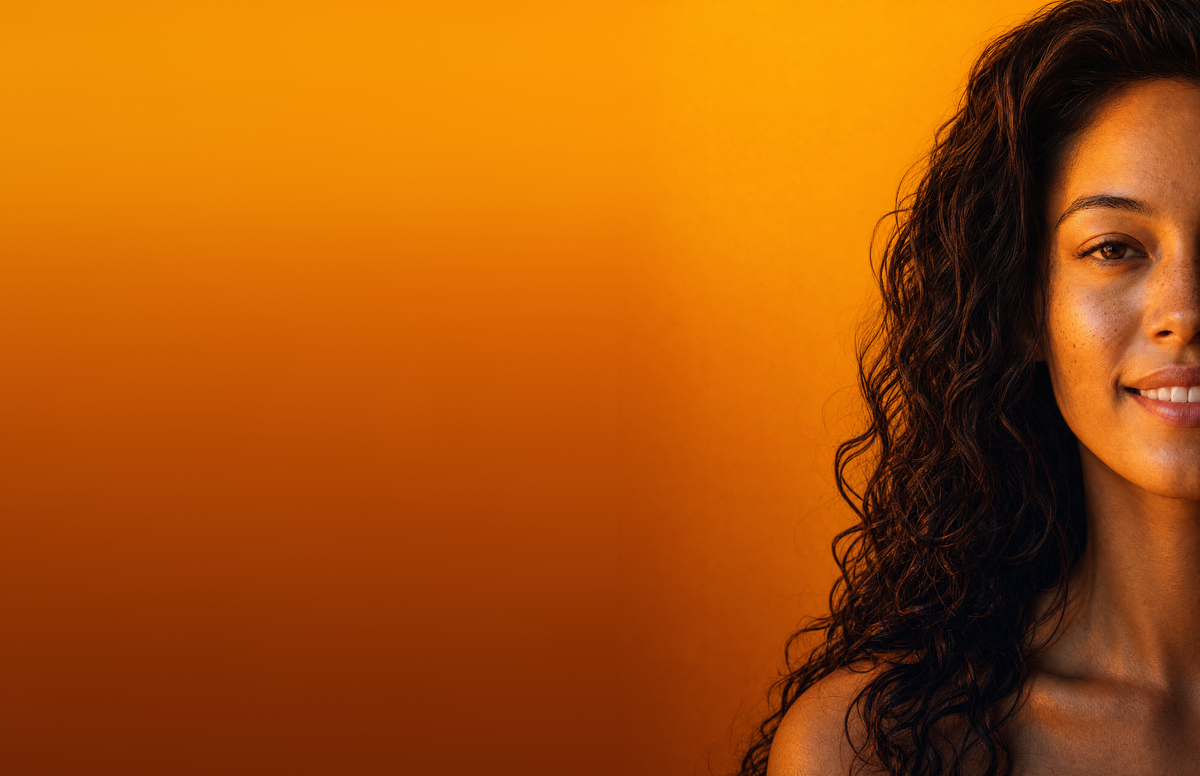 Portrait of a woman with curly dark hair against a warm orange gradient wall